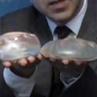 Dr Ricarodo L. Rodriguez holding out 2 different types breast implants in his hands.