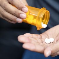 Closeup of woman's hands taking antibiotics out of a prescription medication bottle.