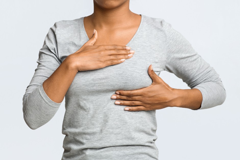Woman in gray shirt performing a breast self-exam, illustrating consideration of breast enhancement options.